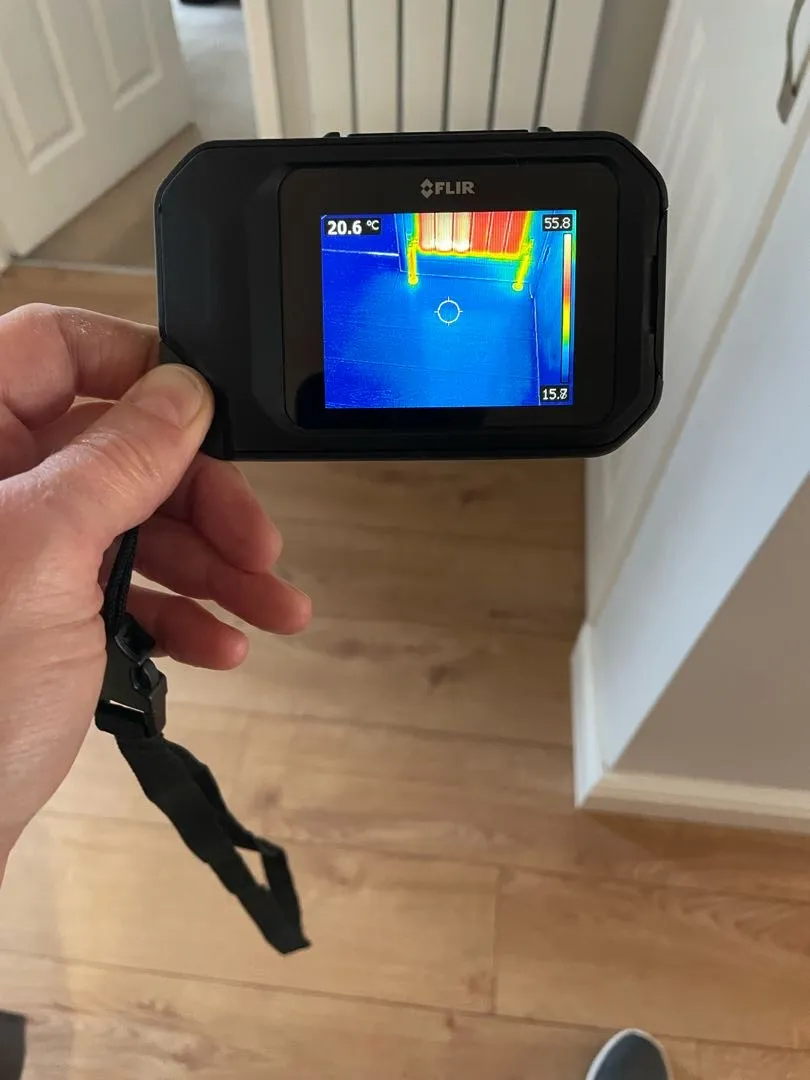 Handheld thermal camera displaying heating pipes and a radiator